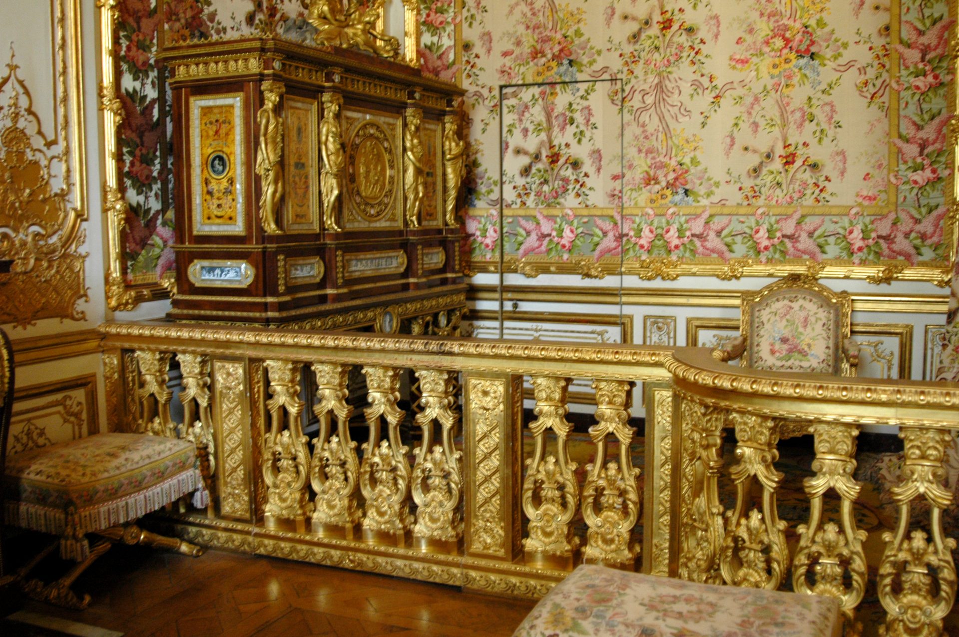 A photograph of a room at Versailles Palace, covered in ornamental gold with a visible secret door in one of the walls.