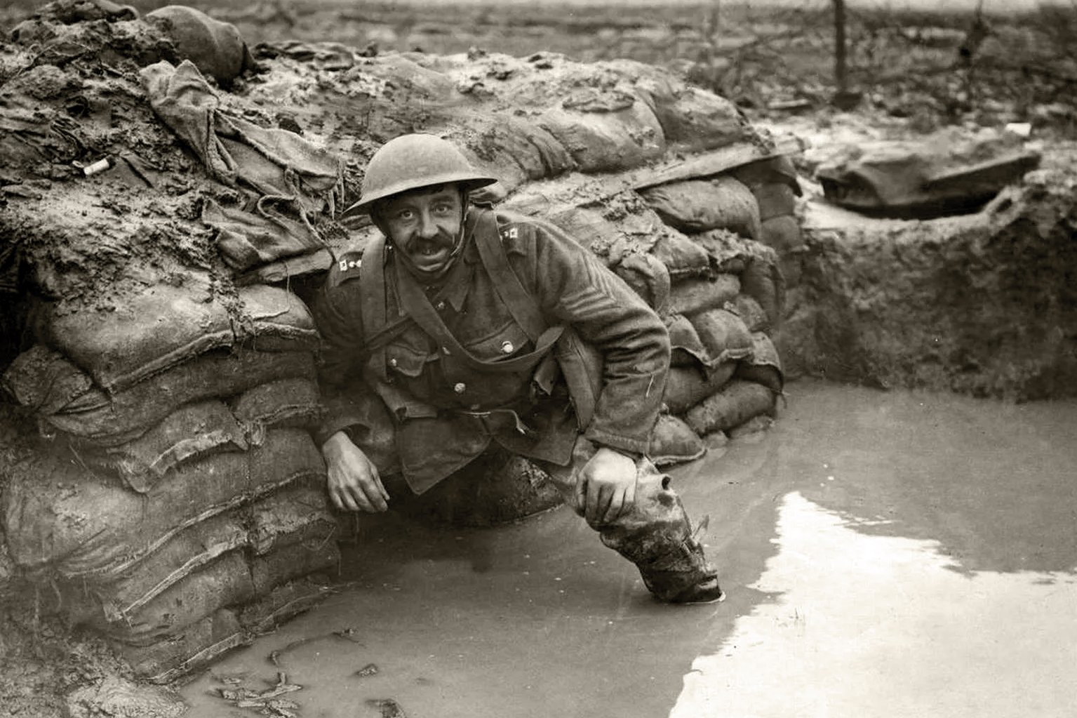 A black and white photo of a soldier in a flooded trench during World War II.