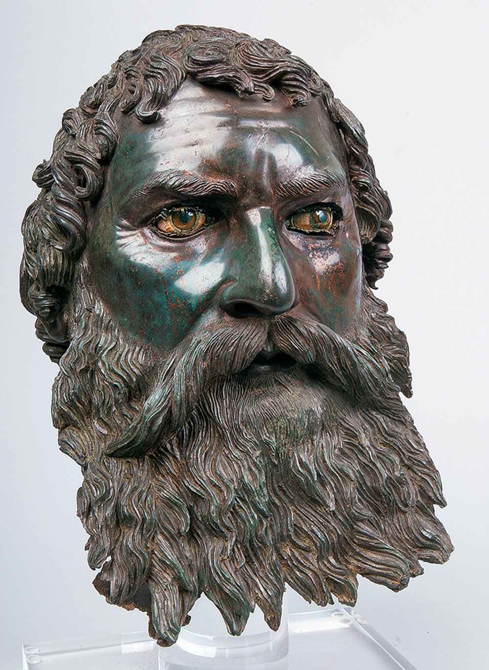 Bronze portrait bust of Seuthes III from around 310-300 BC. The detailed sculpture showcases a powerful visage with intense, inlaid eyes, a pronounced nose, and a richly textured beard and curly hair. The patina of the bronze exhibits shades of green and brown, indicating its age and preservation.