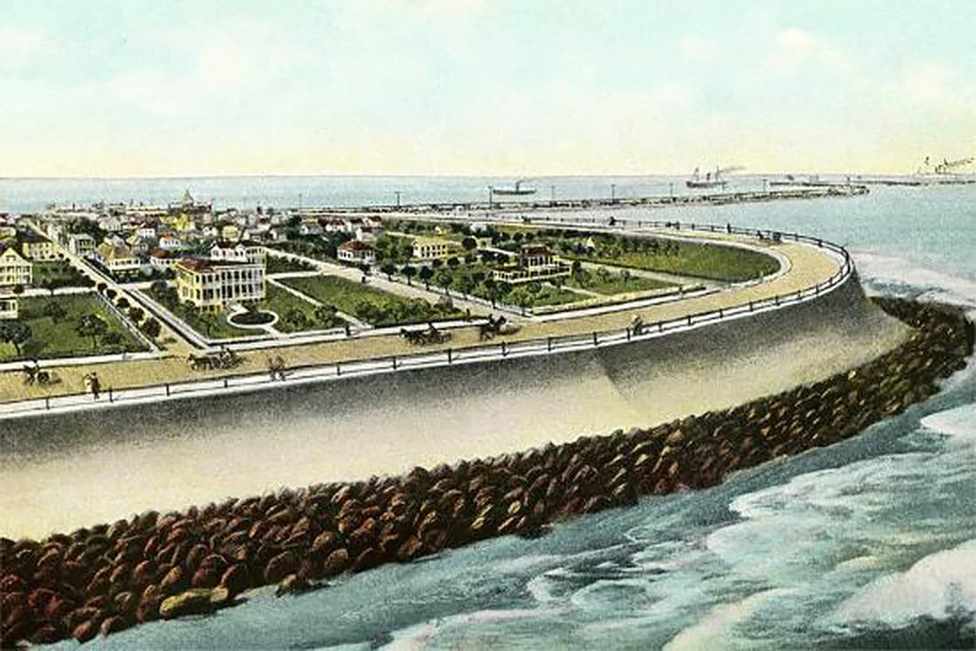 Postcard view of Galveston's 17-foot high Seawall with the city elevated to its top. Ships sail in the distance, and the seawall's 5-mile stretch serves as a scenic boulevard, drawing global visitors.