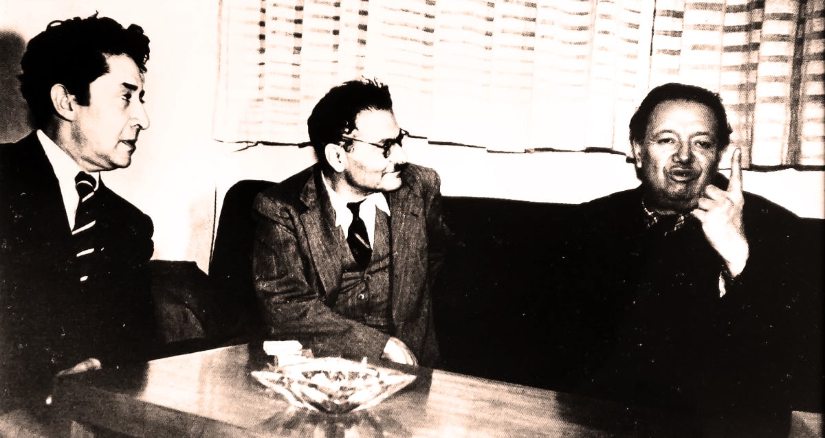 A photograph of Diego Rivera, David Alfaro Siqueiros and José Clemente Orozco wearing suits and sitting around a table with an ashtray.