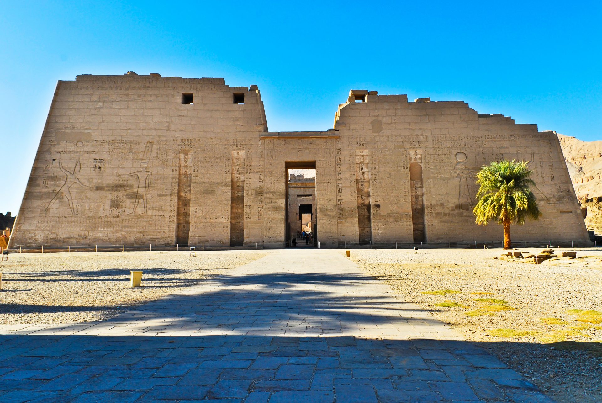 Photo of Medinet Habu, the large and well-preserved Mortuary Temple of Ramesses III in Luxor, Egypt, with towering ancient walls adorned with carvings and hieroglyphs, depicting historical scenes including the pharaoh's triumph over the Sea Peoples.