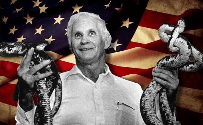 A composite image featuring George Hensley prominently holding snakes against a backdrop of the American flag. Hensley, dressed in a white shirt, gazes upwards, with a serene expression. The snakes he holds coil around his hands, with one snake poised with its head raised. The American flag in the background displays stars and stripes in varying shades of red, white, and blue, symbolizing the cultural context of snake-handling churches in America.