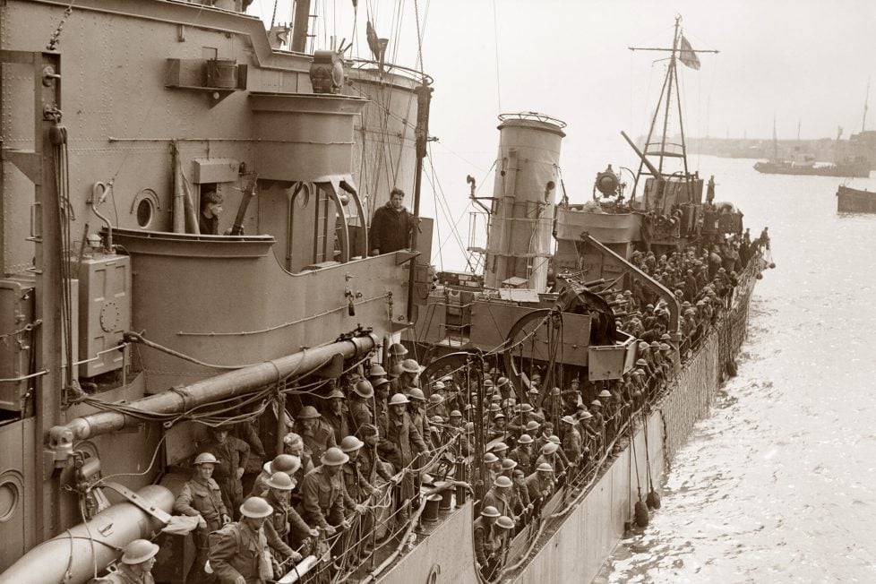 Black and white photo of weary British troops densely packed on the deck of a naval destroyer, returning to Dover after the Battle of Dunkirk, symbolizing the critical evacuation and the questions surrounding the German failure to prevent their escape.