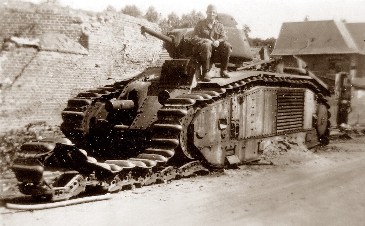 A sepia-toned historical photograph depicts a German soldier seated atop a disabled French Char B1 tank. The tank’s left track is visibly detached and splayed out onto the street, indicating it has been de-tracked. The backdrop features a damaged brick wall and buildings, suggesting a scene from a wartime urban environment. The soldier's posture and expression convey a sense of pride and conquest.