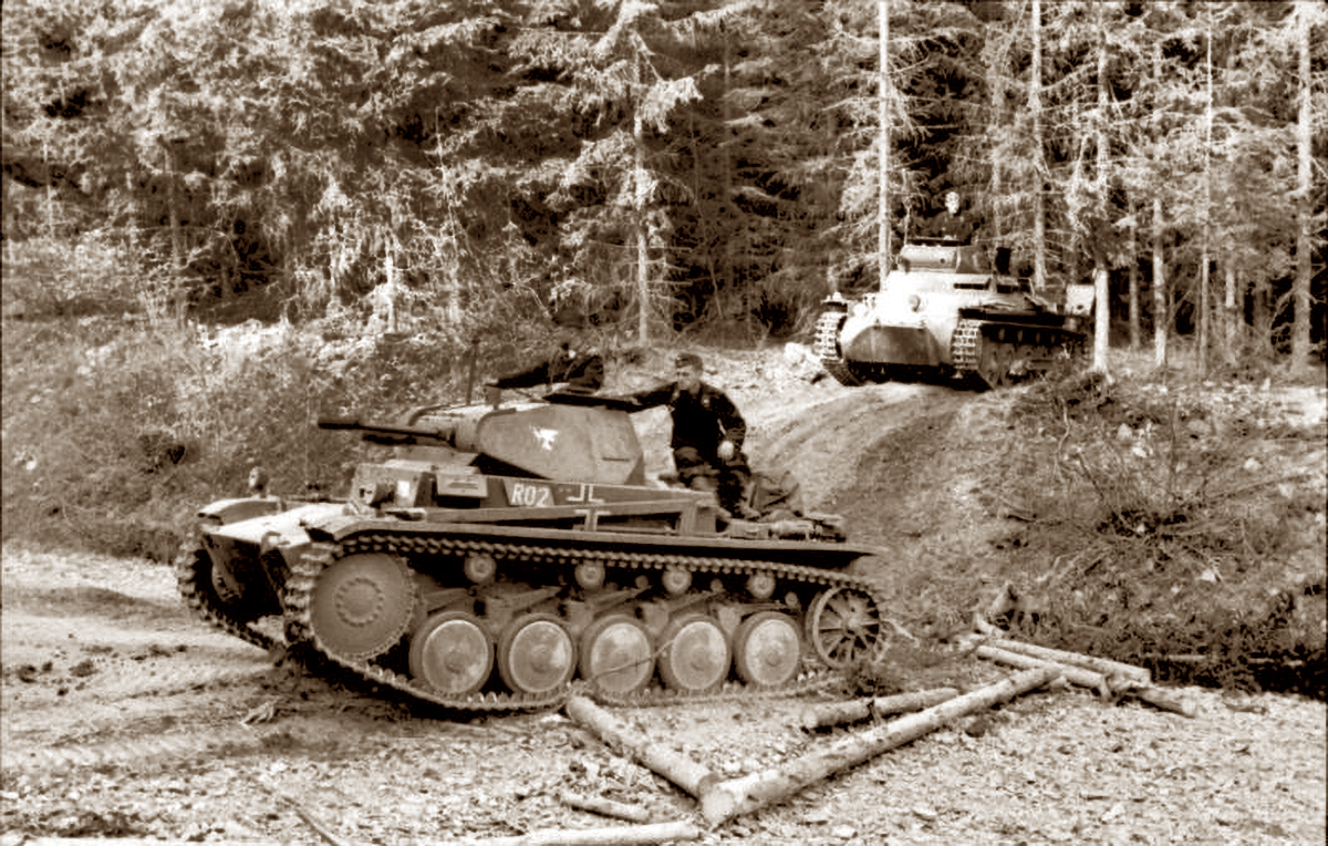 A vintage sepia photograph captures two German tanks, a Panzer II in the foreground and a Panzer I in the background, maneuvering through a forested area. Soldiers can be seen operating the tanks on a dirt path amidst dense trees, illustrating a typical scene of military deployment in a woodland setting during World War II.